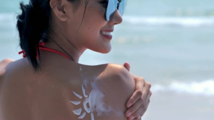 美丽的年轻亚洲女性在海滩上使用防晒霜。慢动作