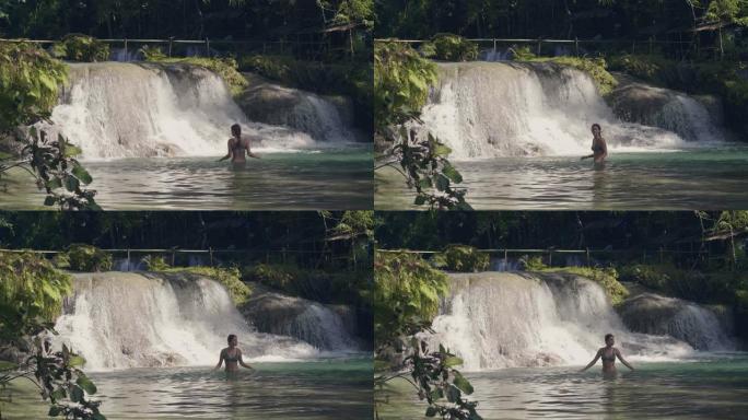 年轻女子沐浴在热带森林的瀑布中，水流溅到背景上。从丛林森林中的瀑布流淌在山河中的石头上。