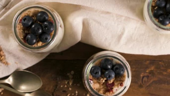 酸奶冻糕配蓝莓和格兰诺拉麦片。健康早餐概念放在梅森罐子里，木桌上有装饰勺子。