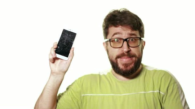 坏掉的小工具的概念。一个大胡子的人展示了屏幕破裂的智能手机。他绝望地诅咒并生气。