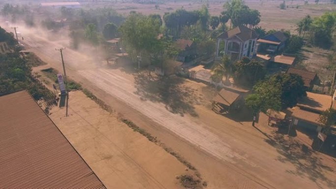 穿过小村庄的尘土飞扬的道路上的车辆的空中静态视图