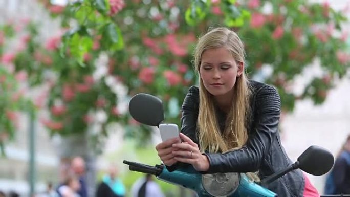 可爱的年轻女子骑着踏板车看着手机