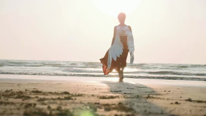 美丽的女天使在日落时赤脚走向大海。