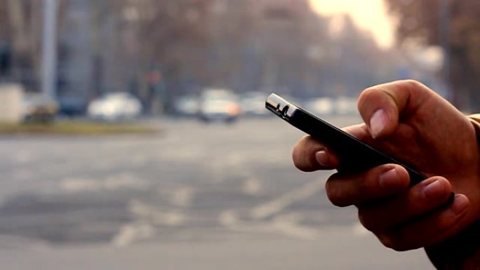 一个男人的手在带有汽车的背景城市景观上使用黑色智能手机