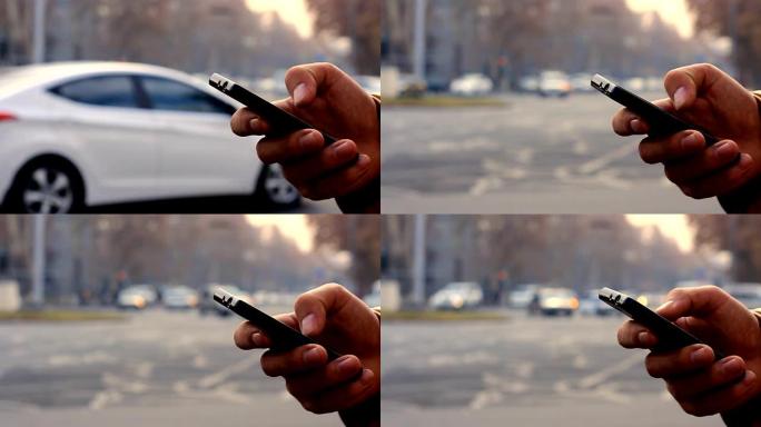 一个男人的手在带有汽车的背景城市景观上使用黑色智能手机