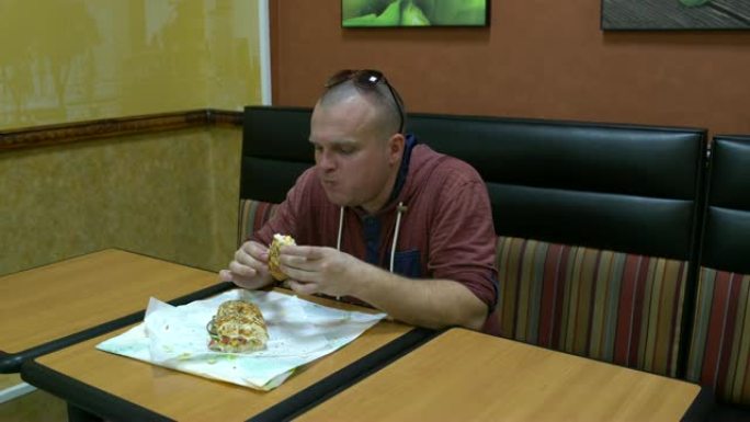 咖啡馆里的男人坐在桌子旁吃三明治。