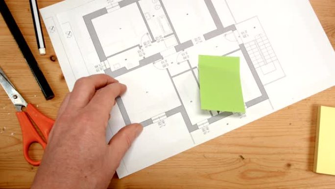 从上方看，室内设计师的手将绿色贴在新房子的技术图纸上，这是建筑物翻新，设计，新房和家庭等主题的理想镜