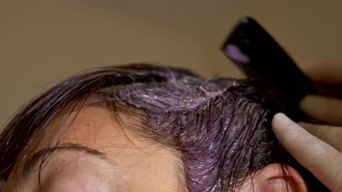 特写美发师在女人的头发上涂上染发剂