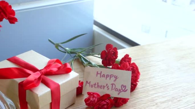 年轻女子系蝴蝶结包装手工制作的精美礼盒母亲节礼物在家用红色康乃馨花束隔离在木桌上，特写特写概念