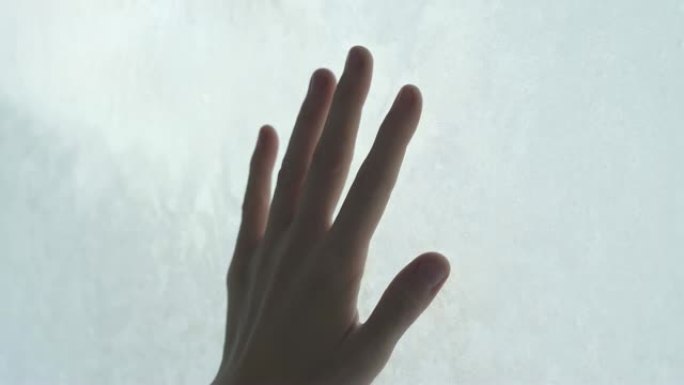 等待新年的少年将手掌放在冰冻的窗户上。窗户上有手的痕迹后