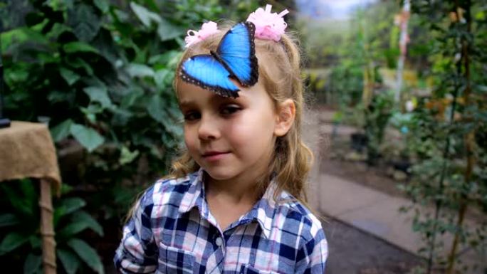 女孩的头上坐着一只美丽的蓝色蝴蝶。女孩正看着镜头，微笑着。4k慢速移动