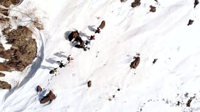 一群游客在同一条路径上相互跟随，在石岩和雪堆之间，空中