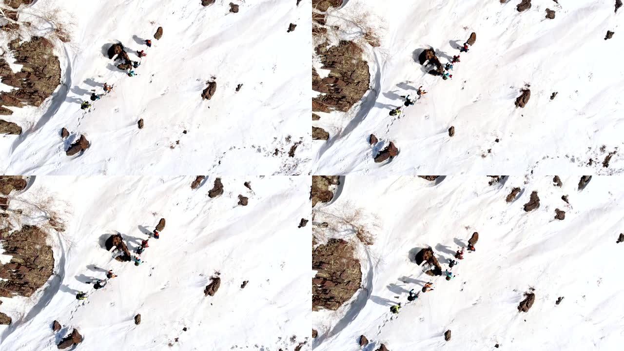 一群游客在同一条路径上相互跟随，在石岩和雪堆之间，空中