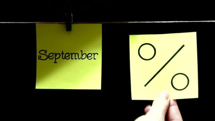 两个彩色贴纸。左边有一张纸上写着“九月”。在右边的黄页上是百分比符号。黑色背景。