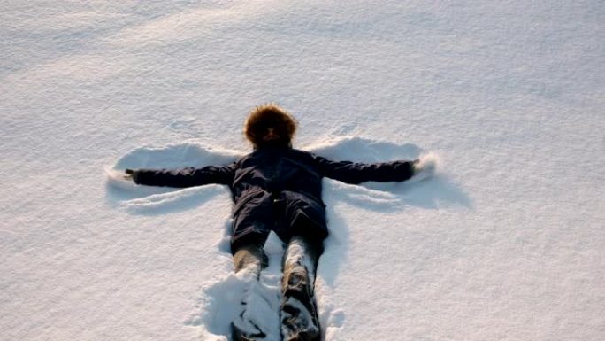 穿着蓝色羽绒服的男人和毛皮兜帽做了一个雪天使。