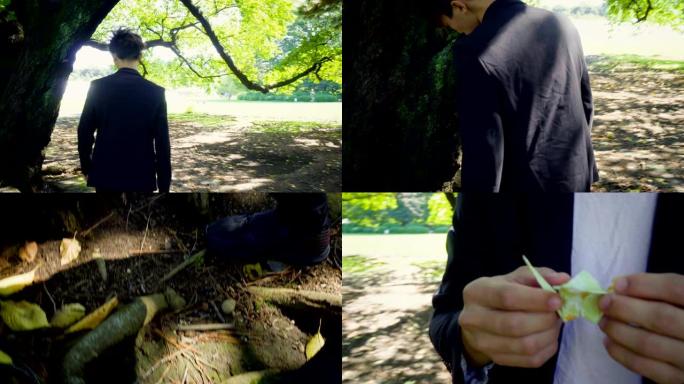 电影-穿着西装的年轻亚洲男子步行到树上从地板上捡起折纸鸟