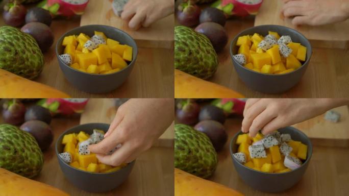 一个年轻女子将火龙果块放入灰色陶瓷碗中拍摄的2倍慢动作镜头，桌子上放着许多热带水果