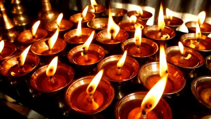 在寺庙里燃烧蜡烛。看到金色闪亮的碗，上面燃烧着油蜡烛的火焰，用于崇拜。