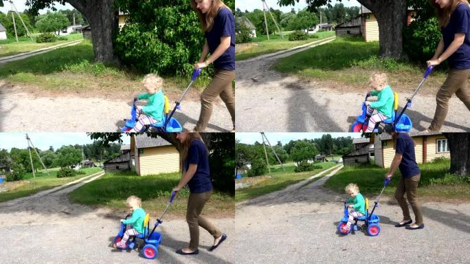 年轻女子母亲在小三轮车上推着金发碧眼的蹒跚学步的女孩。