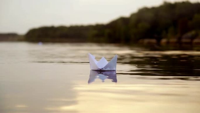 白纸船在傍晚的森林背景附近漂浮在水面上。