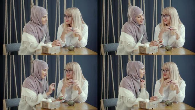 穆斯林妇女正在咖啡馆与她的金发朋友愉快地聊天，喝茶