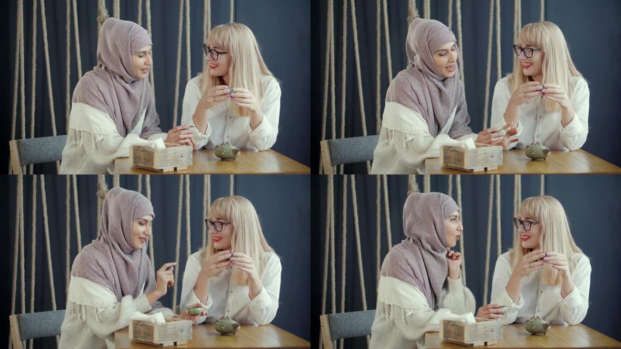 穆斯林妇女正在咖啡馆与她的金发朋友愉快地聊天，喝茶