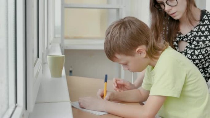 男孩坐在桌子旁学习写信。和他妈妈一起做作业。