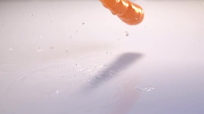 胡萝卜落在白色背景的白色桌子上的水中。慢动作240 fps