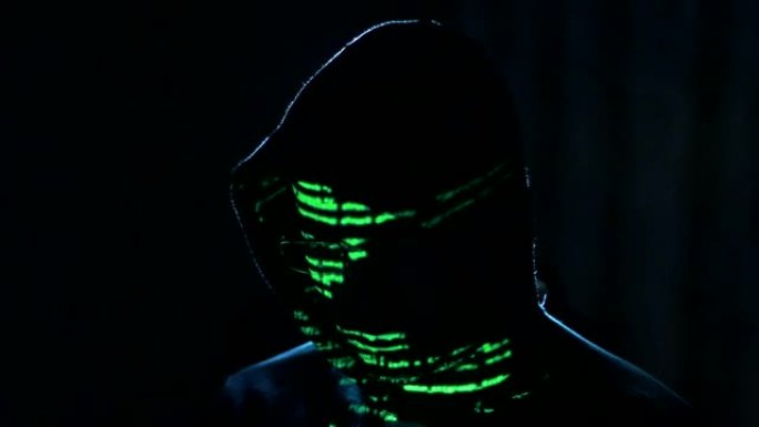 男性黑客在计算机上工作，而绿色代码字符在他的脸上反射