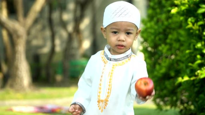 穿着传统服装的开朗的穆斯林小男孩试图自己吃苹果