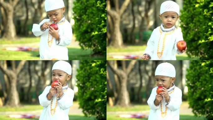 穿着传统服装的开朗的穆斯林小男孩试图自己吃苹果