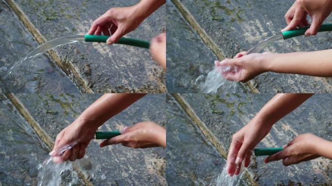 手持花园软管从绿色橡胶管中喷水，并用软管洗手。运动4k镜头