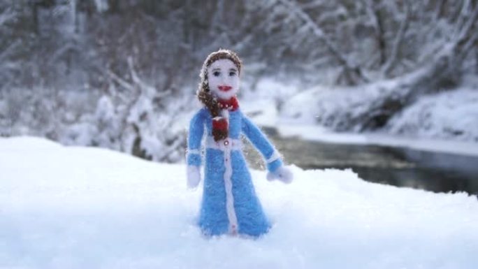 冬季河流背景上站在雪堆里的羊毛制成的玩具女孩