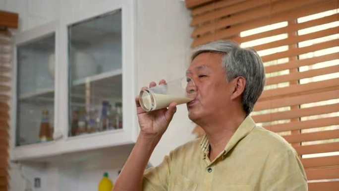 肖像亚洲老人在家厨房喝牛奶。