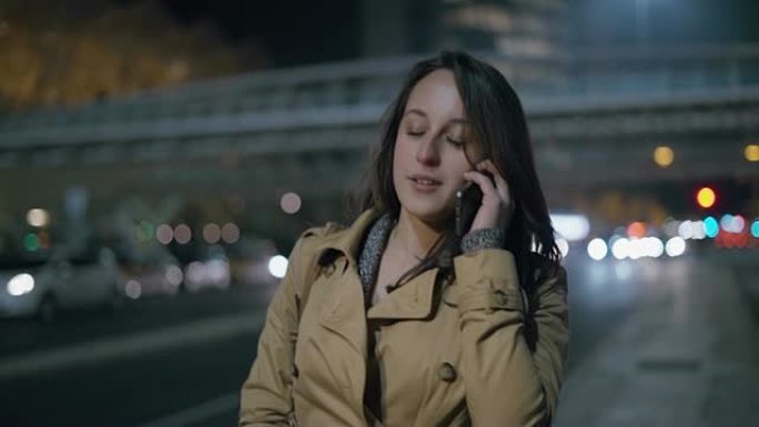 女孩通过智能手机聊天，晚上在城市街道上行走