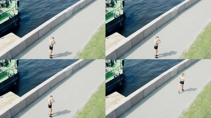 健康的高角度女人沿着河边的路堤慢跑，停下来检查手腕上的健身追踪器并继续比赛