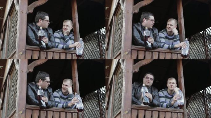 两名男子在露台上喝塑料瓶中的啤酒并讲话
