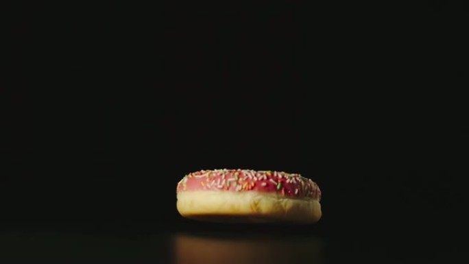 慢动作: 粉红色的甜甜圈落在桌子的黑色表面上