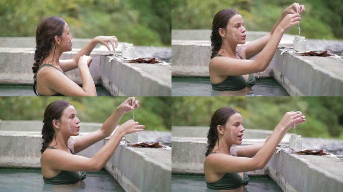快乐的女人洗热水澡，为面膜收集愈合泥。年轻女子在天然水疗中心享受温泉。美容和身体疗法。