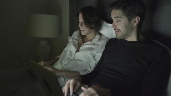 年轻夫妇在床上聊天和使用笔记本电脑