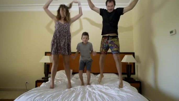 快乐的家庭在床上跳跃。幸福家庭理念。父亲，母亲和小男孩跳到床上