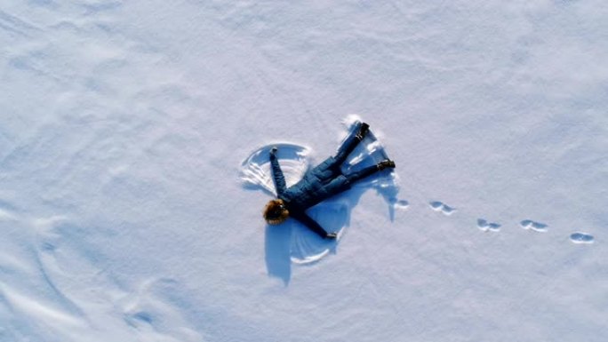 女人让雪天使躺在雪中。航拍视频。