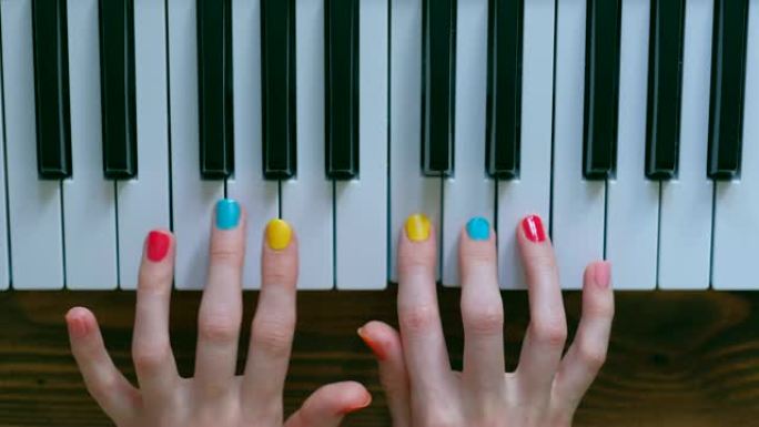一个年轻积极的女孩，有着美丽的手和彩色修指甲，弹钢琴