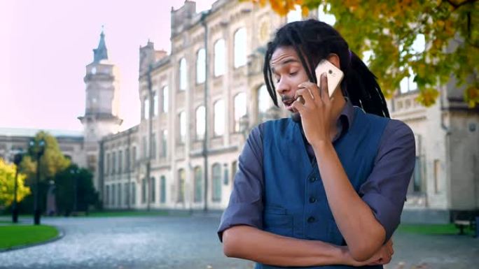 迷人的非裔美国学生的肖像，在大学背景下，长发lock在手机上进行情感交谈。