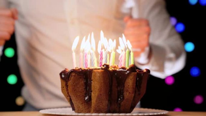 快乐的人在生日派对上跳舞，在美味的巧克力蛋糕前，蛋糕上点着五颜六色的蜡烛