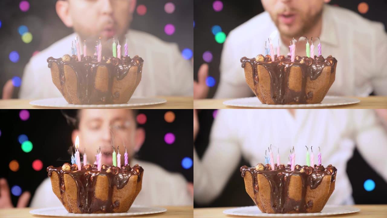 男人快乐地在五颜六色的灯光背景下的生日巧克力蛋糕上吹灭蜡烛。4K