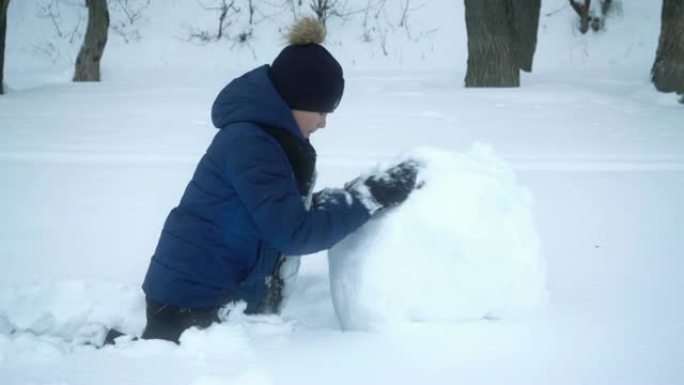 男孩在冬天为雪人滚大雪球。