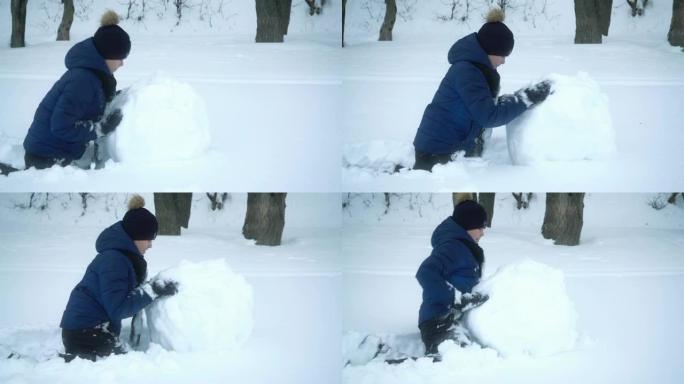 男孩在冬天为雪人滚大雪球。