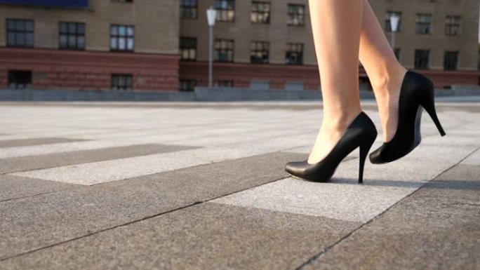 阳光明媚的日子，穿着黑色高跟鞋的苗条女性腿在城市广场散步。穿着高跟鞋的年轻女商人的脚在城市街道上。低