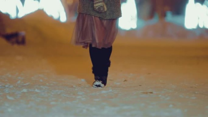 女孩正沿着白雪皑皑的街道行走。女人穿着漂亮的鞋子和裙子。底视图。